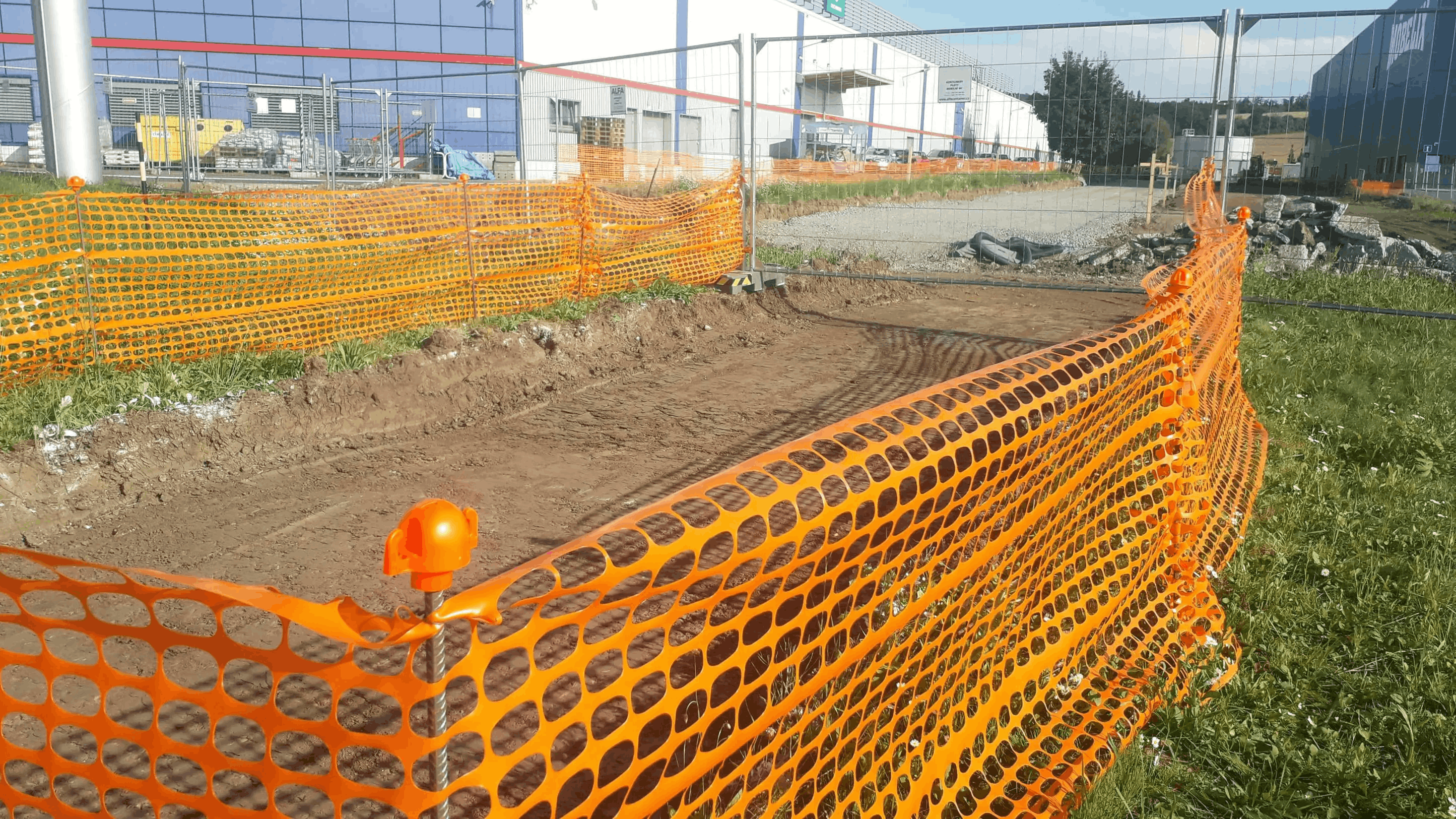 Oranžová plastová vyznačovacia sieť ohraničuje vykopanú jamu v zemi